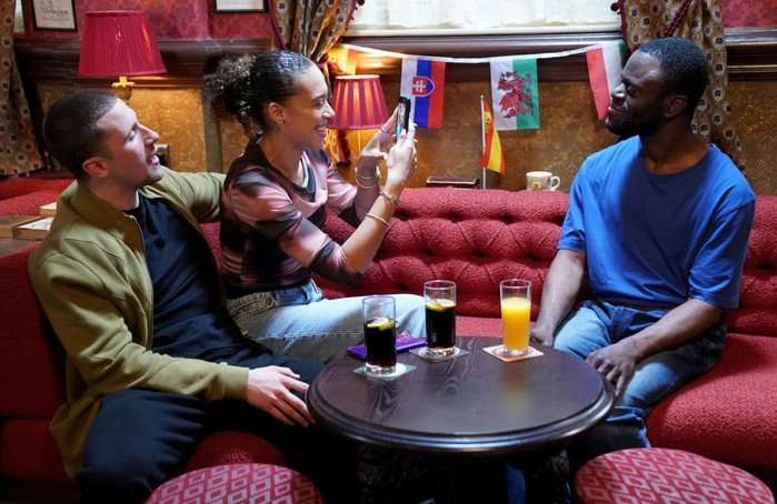 Harry smiles as Gina takes a photo of Kojo in EastEnders