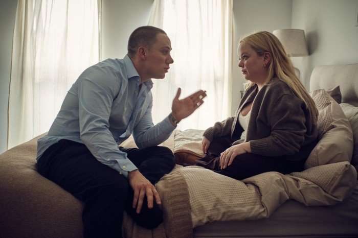 Nicola Coughlan and Joe Cole in I Am Helen, sat on a bed facing each other. He is holding his hand out gesturing at her, as if in an argument.