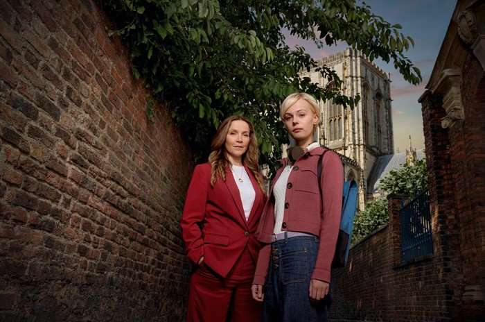 Patience - Series 2 Detective Frankie Monroe (Jessica Hynes) and Patience Evans (Ella Maisy Purvis); they are photographed standing against a red brick wall, with York Minster in the distance behind them