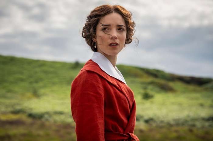 Jessica Reynolds as Emma Harte in A Woman of Substance standing on top of a hill, looking worried as she wears a red blazer and white shirt.