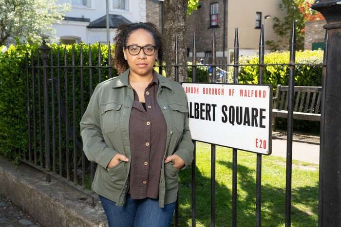 A7R07440 Belinda Owusu as Libby Fox in EastEnders, stood beside the Albert Square sign