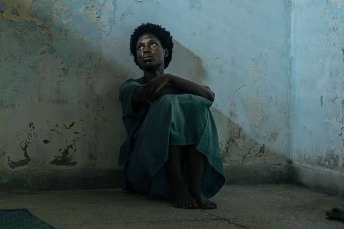AGENCY_201_lv_250702_00684_RT2 Jodie Turner-Smith as Samia in The Agency, wearing grey rags and sat on the floor in a prison cell, looking up at light coming in from the window.