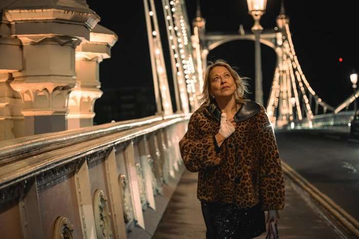 Alice walks down a brightly lit up bridge at night, smiling