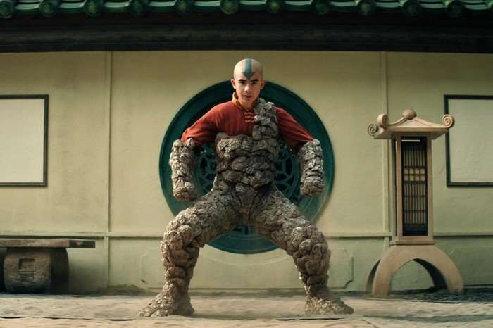 Gordon Cormier as Aang in season 2 of Avatar: The Last Airbender. He's wearing orange robes and his lower body has turned to stone.