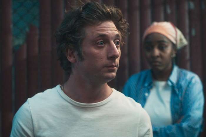 Jeremy Allen White and Ayo Edebiri in The Bear Jeremy Allen White and Ayo Edebiri in The Bear. He is stood in front of a red wall wearing a white t-shirt, while she is wearing a white t-shirt with a blue shirt over the top and an orange bandanna.