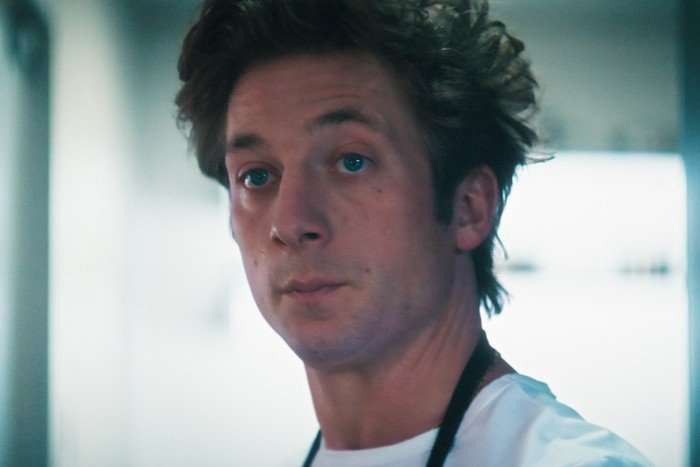 Jeremy Allen White in The Bear, wearing a white t-shirt and blue apron.