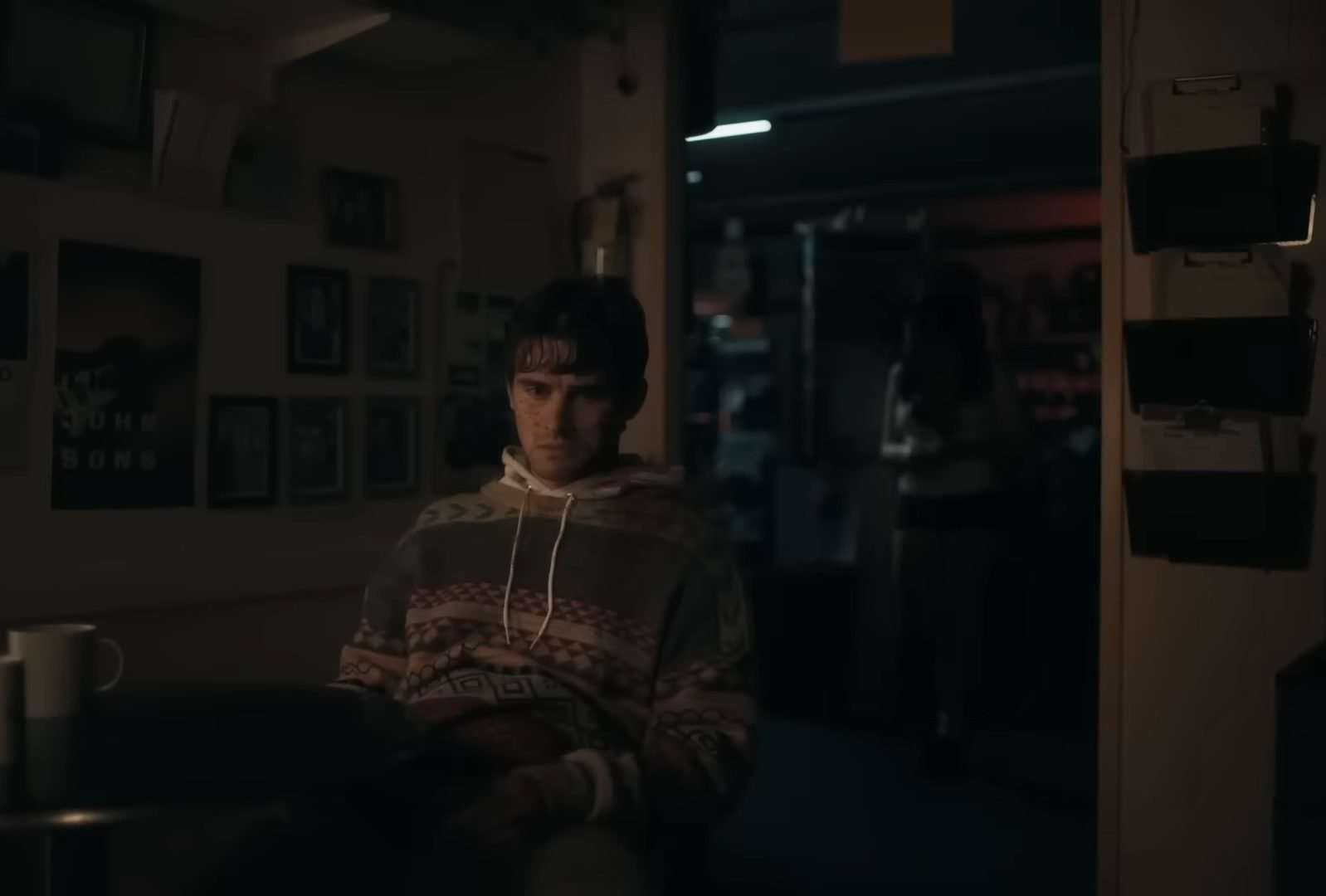 Bear (Michael Johnston) sitting with Nikki (Inde Navarrette) standing behind him in the horror film, Obsession.