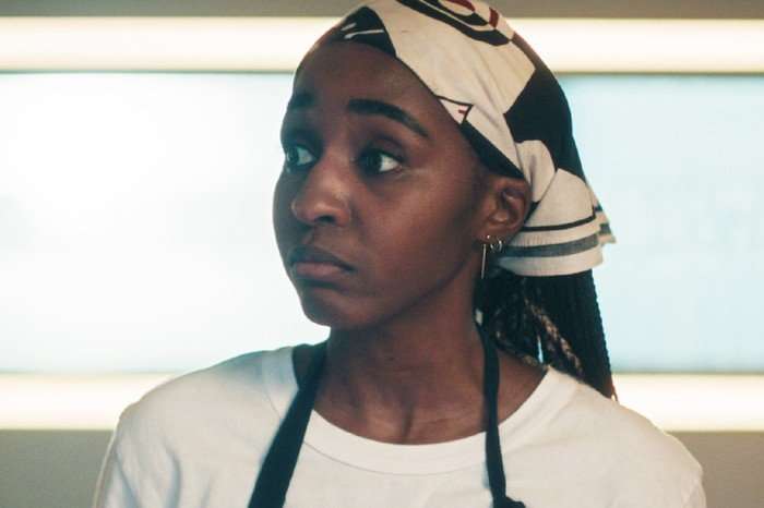 Ayo Edebiri in The Bear, wearing a white t-shirt, blue apron and a bandana.