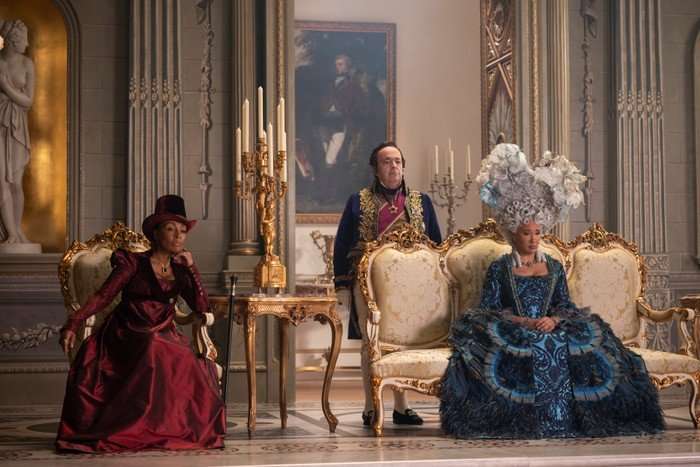 Bridgerton-s4-QueenCharlotte-LadyDanbury Adjoa Andoh as Lady Danbury, Hugh Sachs as Brimsley, Golda Rosheuvel as Queen Charlotte in Bridgerton sitting in a large opulent room in ballgowns, waiting for someone to arrive.