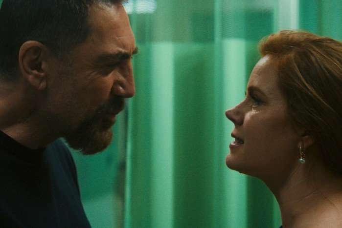 Javier Bardem&rsquo;s Max Cady, with cropped dark hair and a beard, leans in close to a wary Amy Adams in a dim, green-lit corridor scene from Cape Fear (2026).