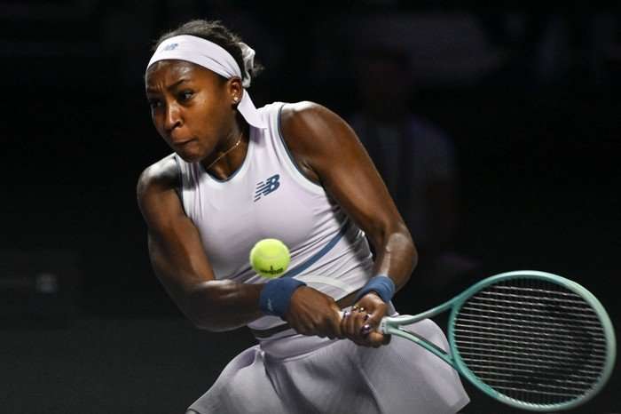 Coco Gauff Coco Gauff, in white tennis kit, hits a two-handed backhand.