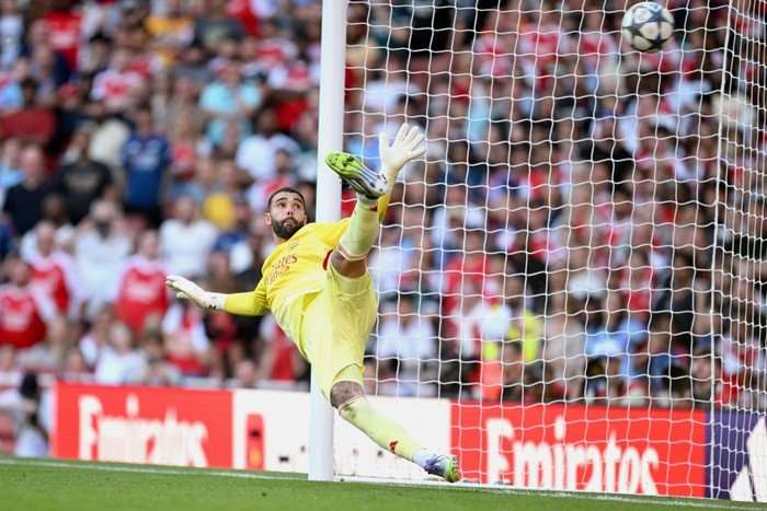 David Raya, in yellow Arsenal goalkeeping kit, looks back at the ball as he makes a save.
