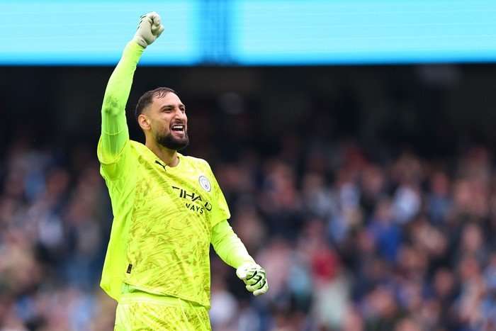 Gianluigi Donnarumma, in yellow Man City goalkeeper kit, smiles as he holds his right fist up in celebration.