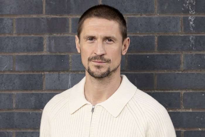 EMBARGO_CORO_CARL_WEBSTER Jonathan Howard poses against a grey brick wall as Carl Webster in a promo shot for Coronation Street.