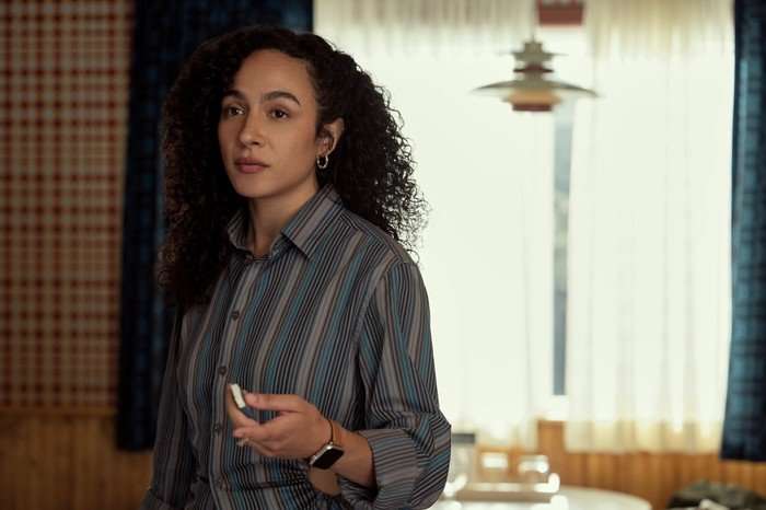 Every Year After Aurora Perrineau as Chantal standing with something in her hand, wearing a striped shirt and looking annoyed.