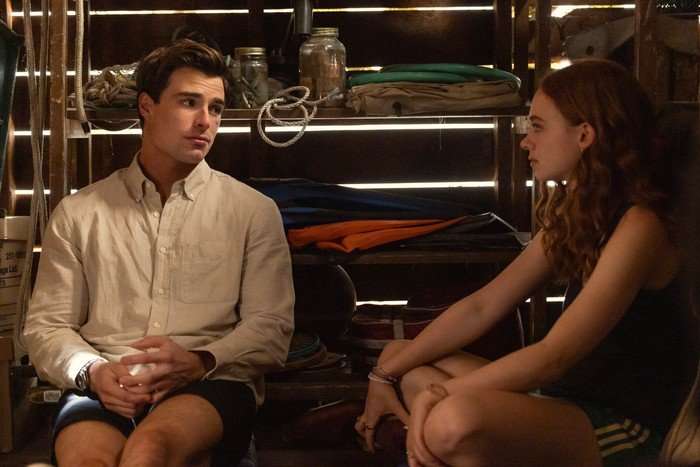 Every Year After Michael Bradway as Charlie Florek, Sadie Soverall as Percy Fraser sitting in a hut with wooden slats, talking to each other.