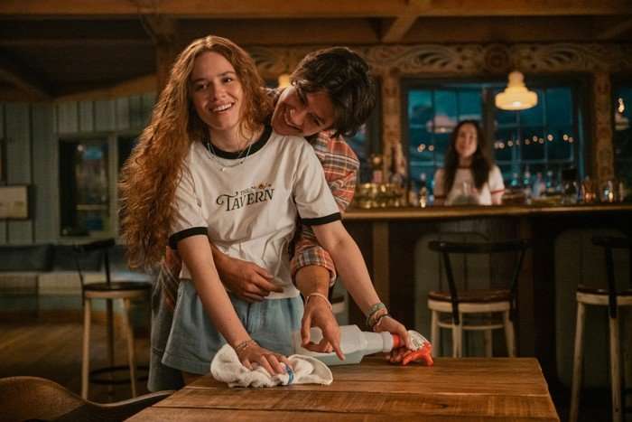 Sadie Soverall as Percy Fraser, Matt Cornett as Sam Florek in Every Year After laughing whilst cleaning a table in an embrace.