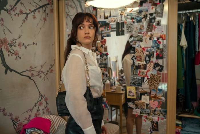 The Girlfriend - First Look Olivia Cooke stars in The Girlfriend; her character is peering over her shoulder, while standing in front of a mirror bordered with dozens of photographs