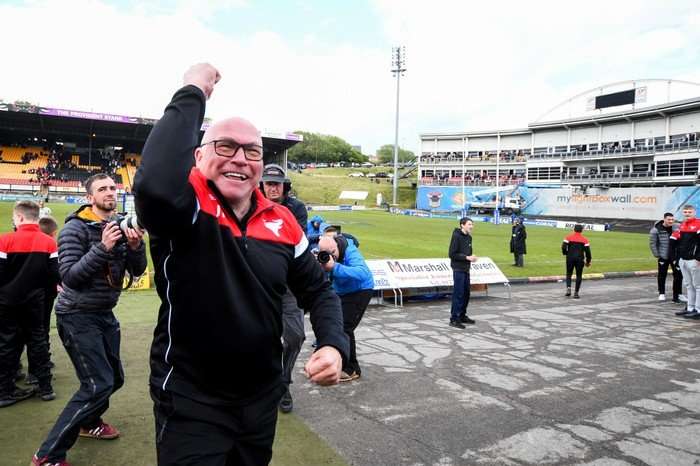John Kear John Kear, in a red and black Bradford Bulls jacket, smiles as he raises his fist in celebration.
