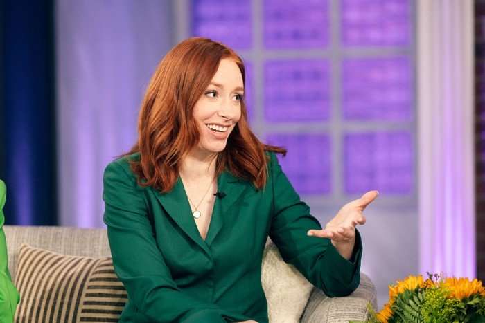 Hannah Fry sat down on a sofa wearing a green pant suit smiling ahead.