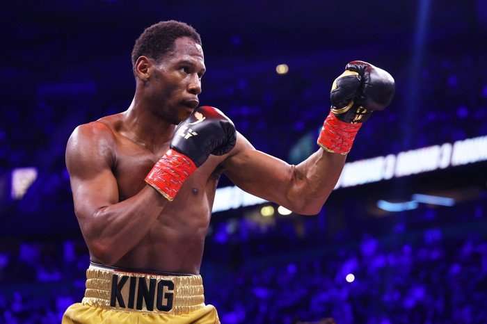 A topless man wearing boxing shorts with his fists in the air.