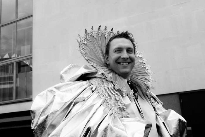 Joe Lycett in a black and white image, smiling as he looks across from him.