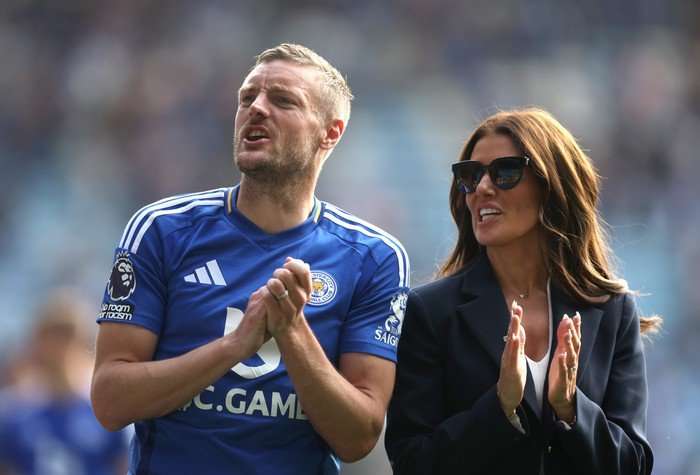 Jamie and Rebekah Vardy stood next to each other clapping as they walk along a football pitch.