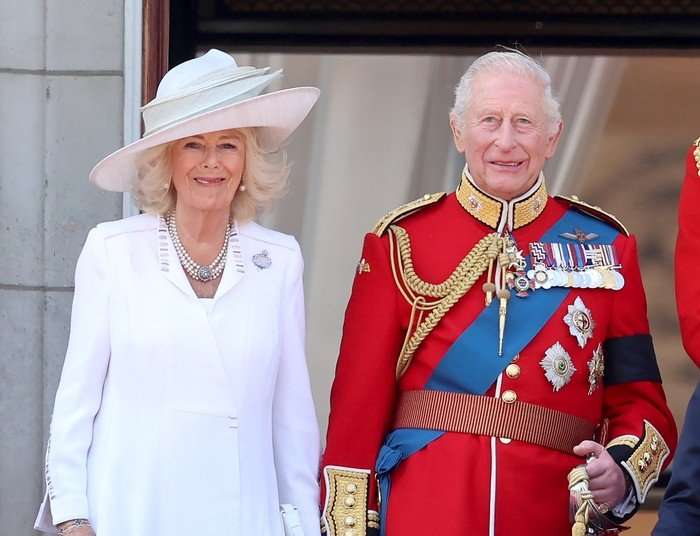 Trooping The Colour 2025 Queen Camilla and King Charles III stood wearing regal attire on the balcony of Buckingham Palace, smiling ahead.