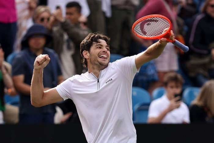 Tennis player Taylor Fritz, in white, smiles and punches the air with his racket in the other hand at Eastbourne.
