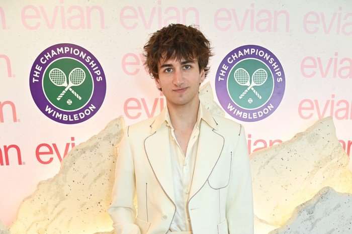 Sebastian Croft wearing an all white suit smiling ahead as he poses for a photo.