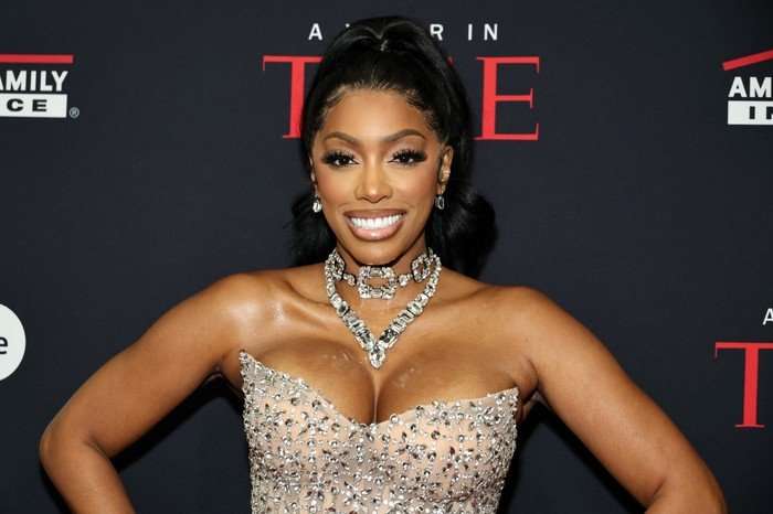 the-traitors-US Porsha Williams smiling ahead wearing a bedazzled sleeveless gown and statement jewel necklace.