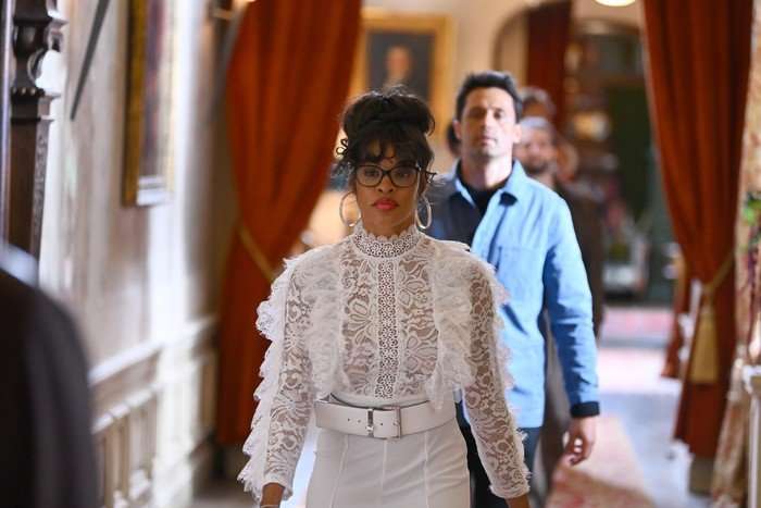 the-traitors-US Tiffany Mitchell wearing a white lace dress, walking through the corridor on the The Traitors castle and looking ahead.