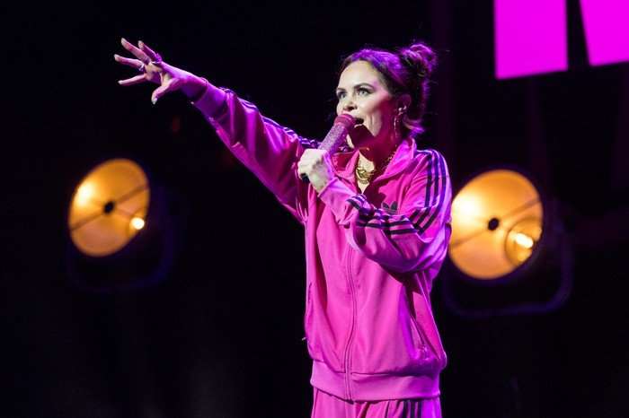 Joanne McNally stood on stage holding a microphone to her mouth with her other hand in the air.