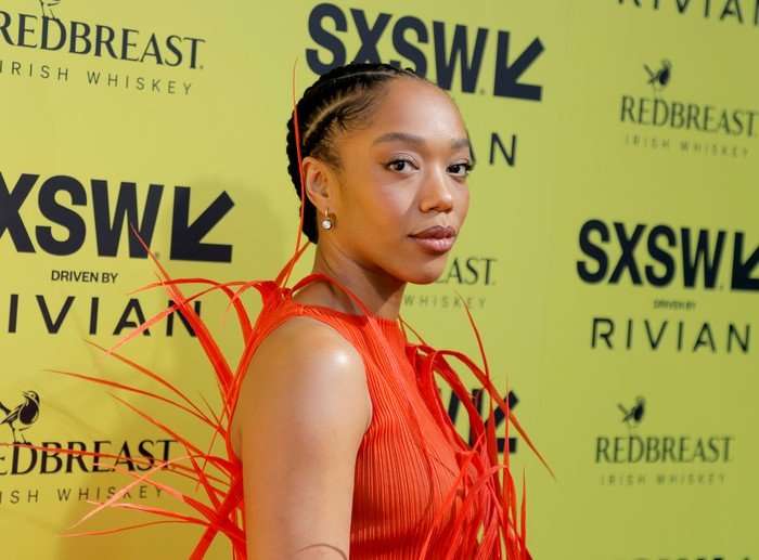 "I Love Boosters" Premiere - 2026 SXSW Conference And Festival Naomie Ackie stands in an orange dress with spiky detailing in front of a yellow SXSW sign