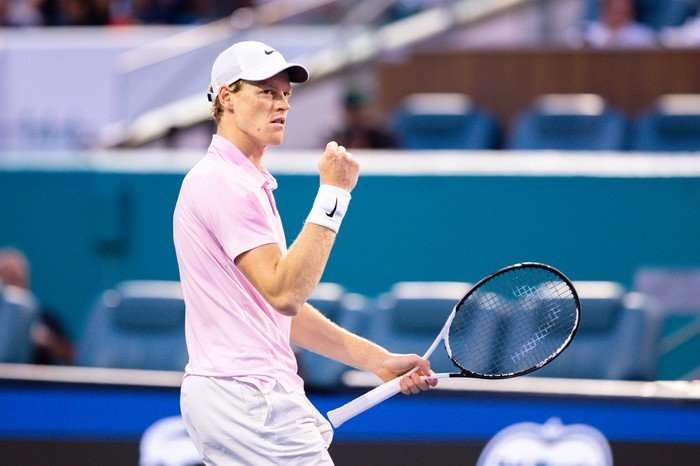 Jannik Sinner Tennis player Jannik Sinner, in a white cap, pink polo and white shorts, raises his fist in celebration on court at the Miami Open.
