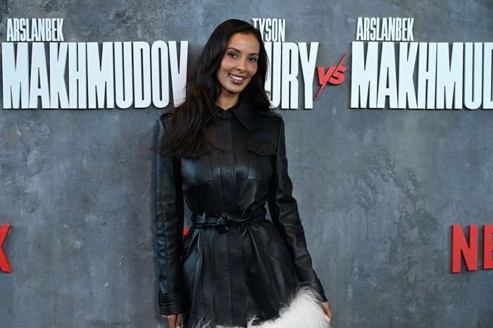 Maya Jama wearing a black dress, smiling ahead as she poses for a photo on a red carpet.