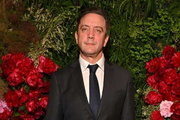 GettyImages-2274474243 Peter Serafinowicz, wearing a black suit and tie, stood in front of a flower wall.