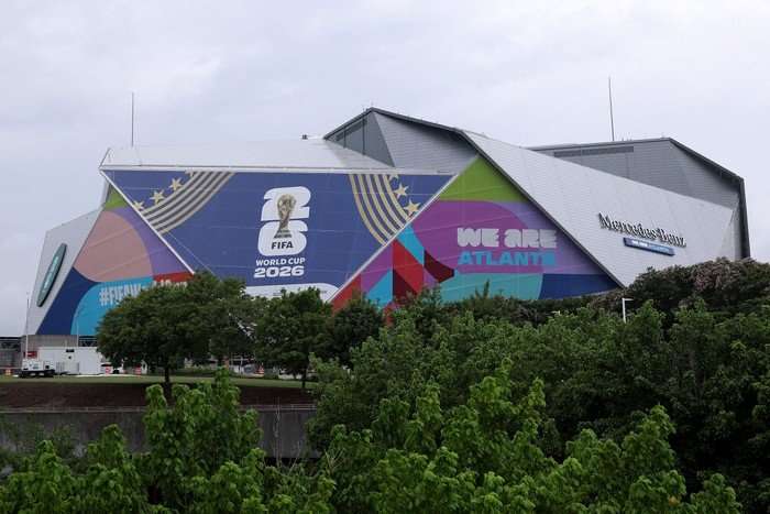 A zoomed out image of the outside of Atlanta Stadium, with World Cup advertising on the side, rises up above trees.