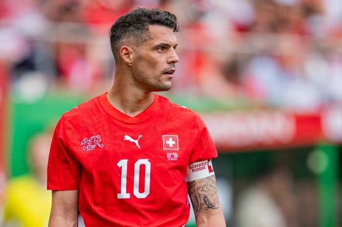 Granit Xhaka Switzerland midfielder Granit Xhaka, in red football kit, stands watching play on the pitch.