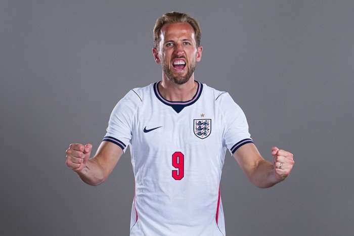 Harry Kane World Cup 2026 England captain Harry Kane, in a white football shirt, shouts and clenches both fists in front of a grey background.