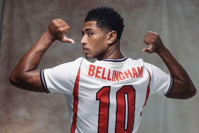 World Cup 2026 England England midfielder Jude Bellingham, in white and red football kit, looks over his shoulder and points to the name and number on his back.