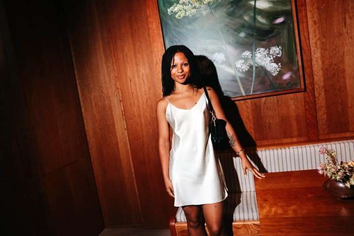 Myha'la wearing a white satin dress smiling ahead as she stands next to a table.