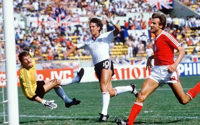 Footballer Gary Lineker in England kit scores a goal as a Polish goalkeeper looks on.