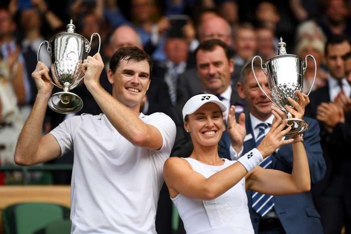 Jamie Murray and Martina Hingis side by side, smiling and holding Wimbledon mixed doubles trophies aloft.