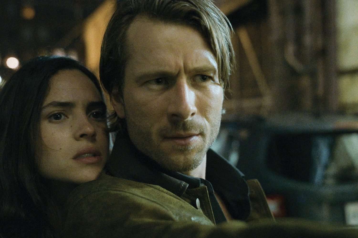 A woman rests her head on a man's shoulder while he poits a gun.