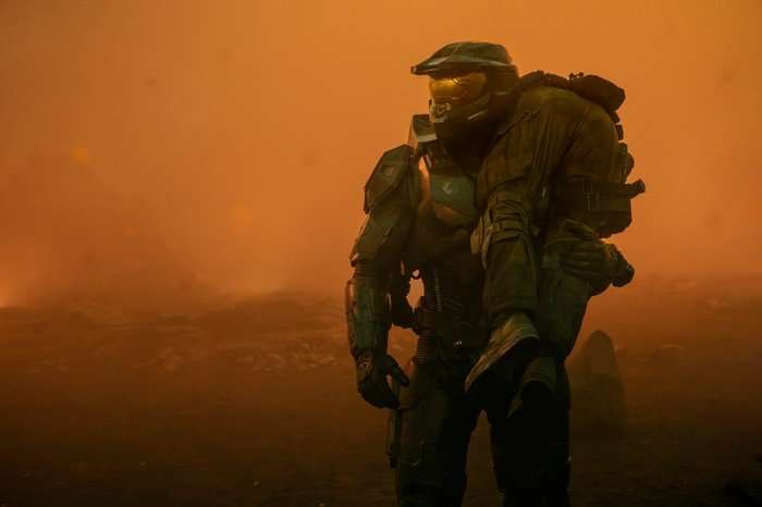 Sanctuary Pablo Schrieber as Master Chief in Halo season 2, holding a person over his shoulder and surrounded by orange light