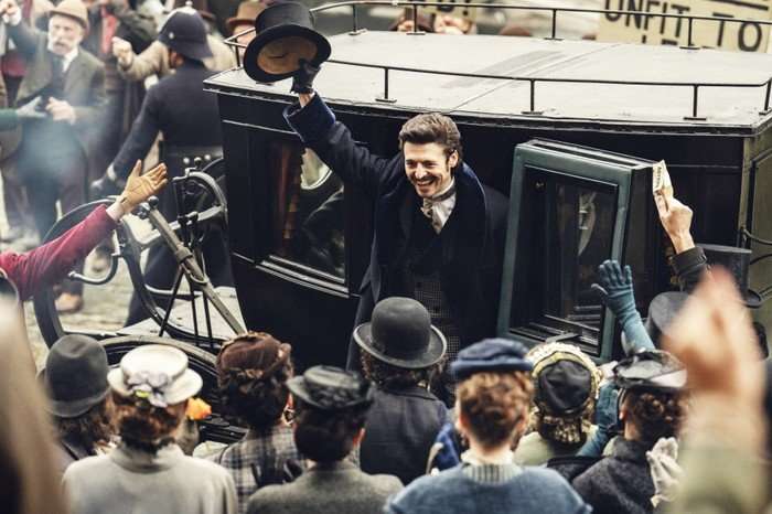 Anthony Boyle as Arthur Guinness, stepping out of a carriage to a crowd of people, wearing a suit, raising his hat