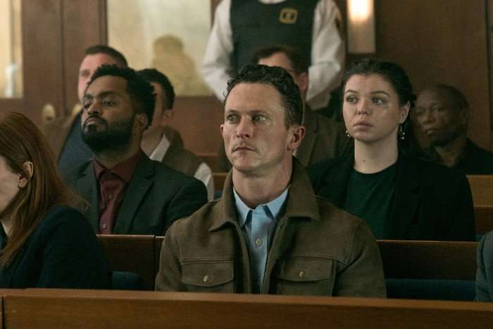 I Will Find You Jonathan Tucker as Adam Mackenzie in I Will Find You sitting in a court room looking wide-eyed and shocked as he sits on a wooden bench.