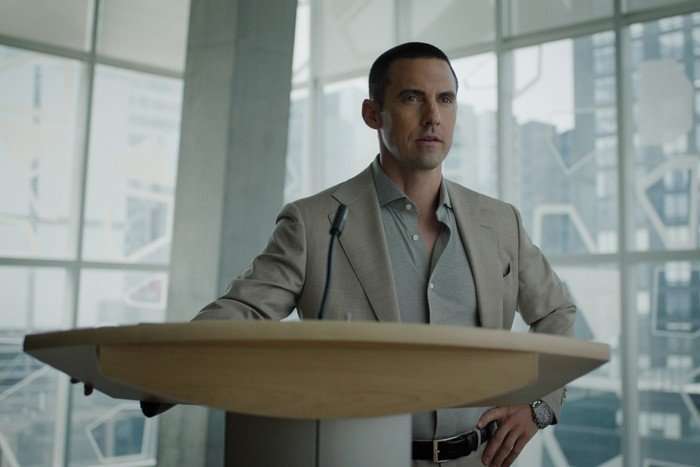 I Will Find You Milo Ventimiglia as Hayden Payne in I Will Find You standing at a wooden plinth, giving a speech whilst stood in a glass office.