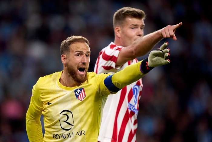 Jan Oblak, in yellow Atletico Madrid goalkeeping kit and white gloves, points and shouts, with a teammate in the background.